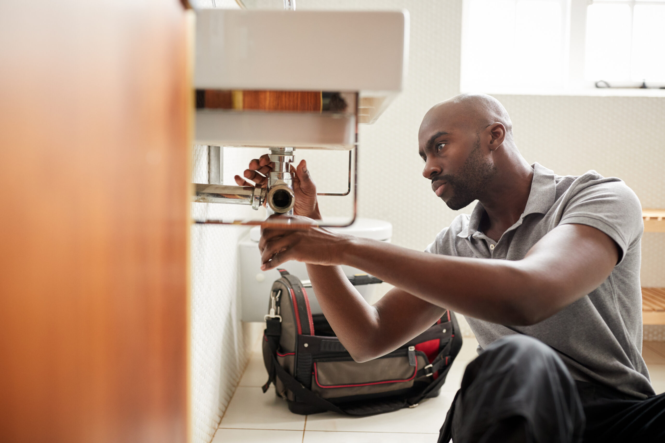 Young,Black,Male,Plumber,Sitting,On,The,Floor,Fixing,A plumber fixing a bathroom